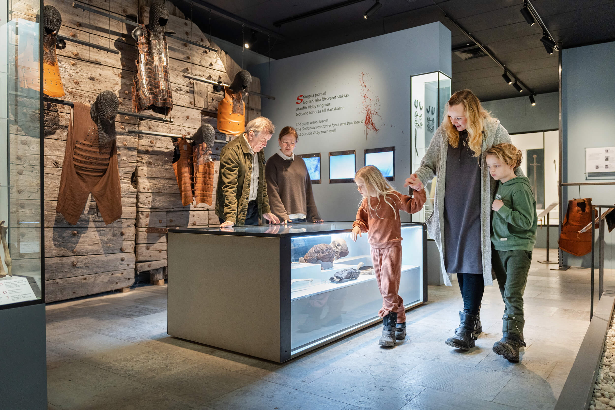 En familj med två barn utforskar en museiutställning med artefakter i en glasmontre, med historiska träföremål monterade på väggen i ett väl upplyst, modernt galleri.