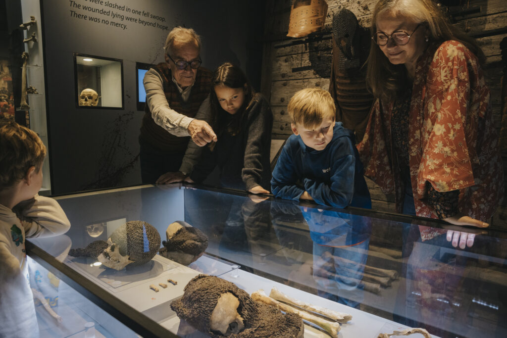 Museum. En man och en kvinna med två små barn står och ser på en monter med skelett i.