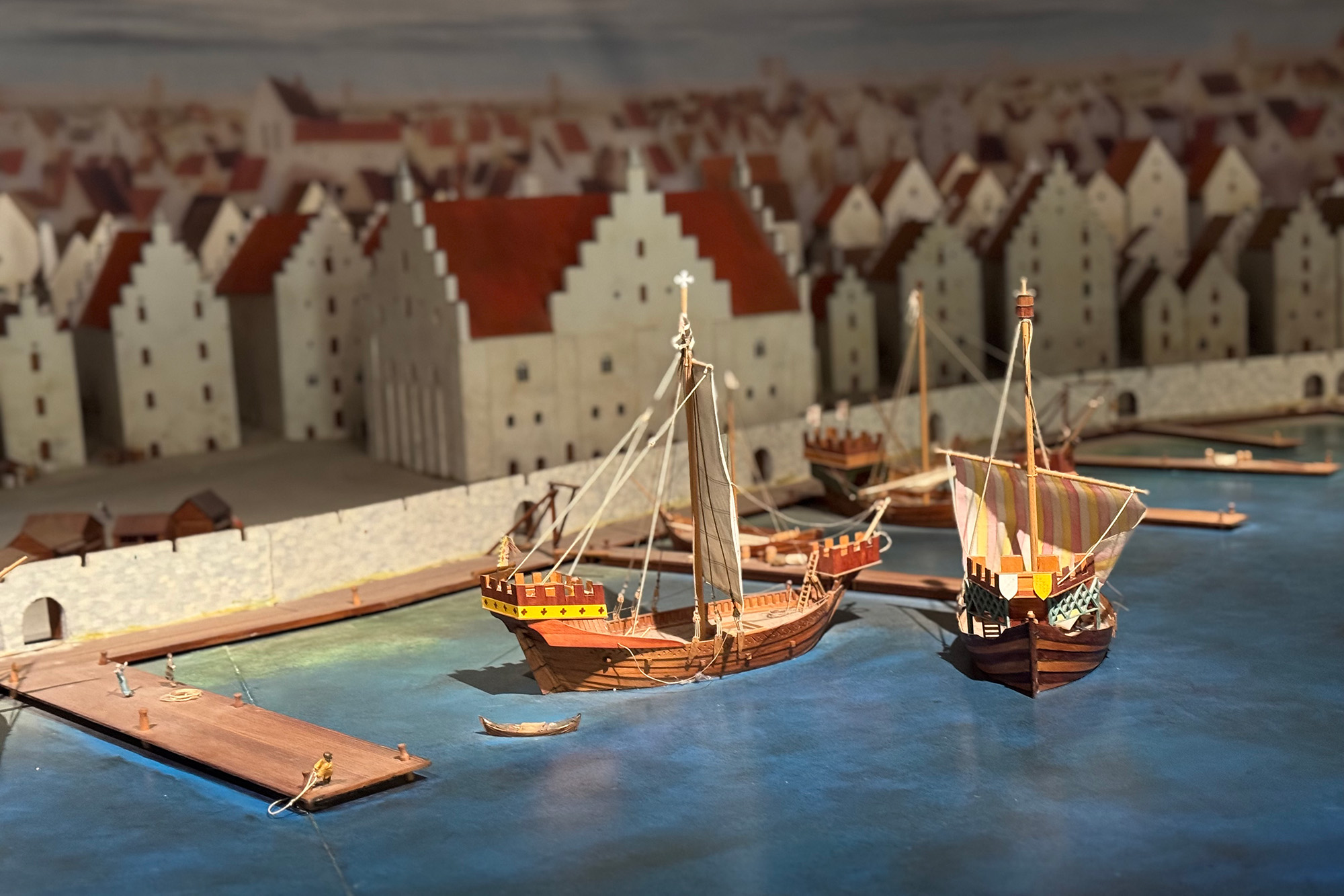 Modell på en stad. Det ,medeltida Visby. Vita hus med trappgavlar. Vatten framför och båtar.