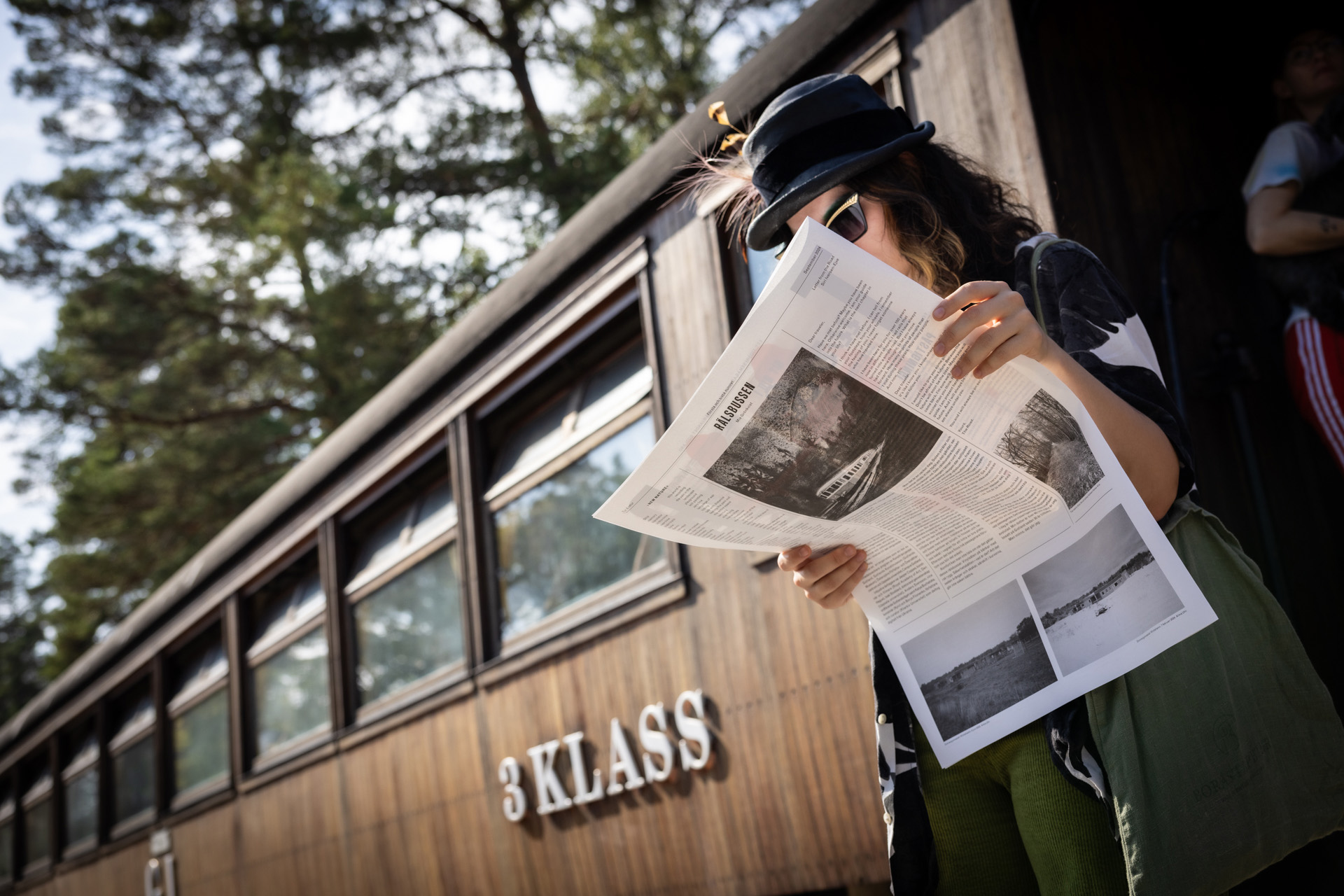 En kvinna utanför en äldre tågvagn. Hon läser en tidning.