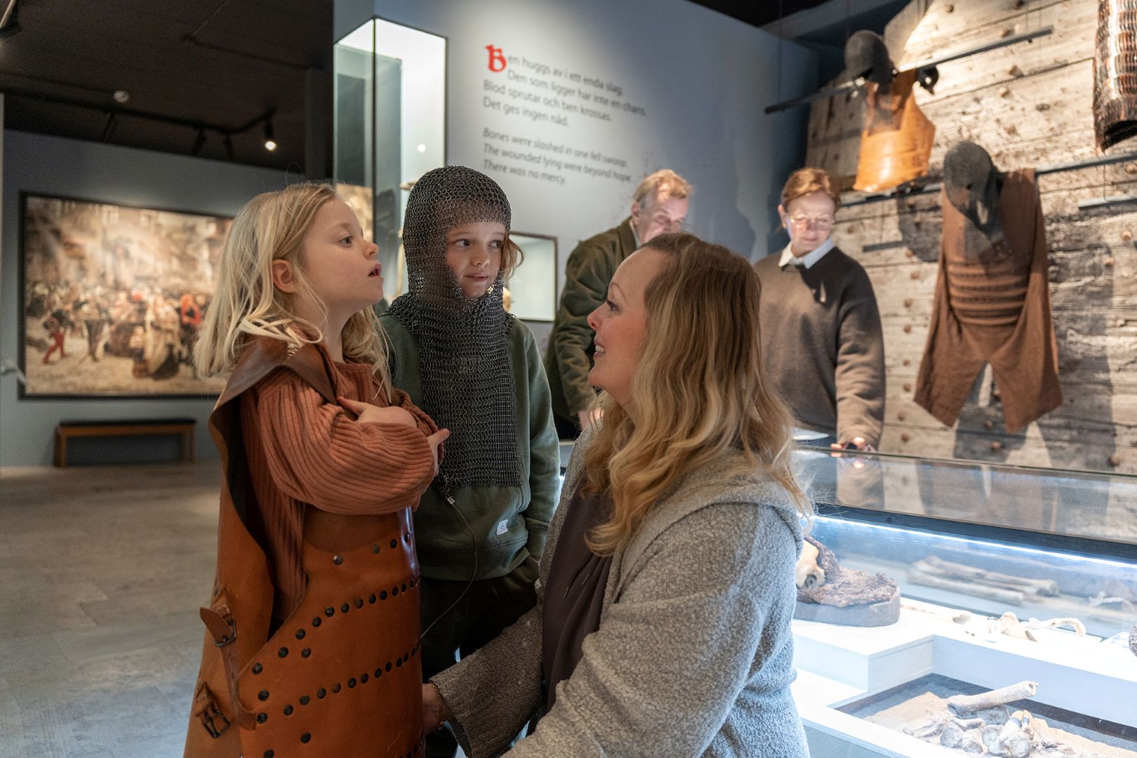 En mamma med två barn. De är på ett museum. Barnen har riddarkläder.