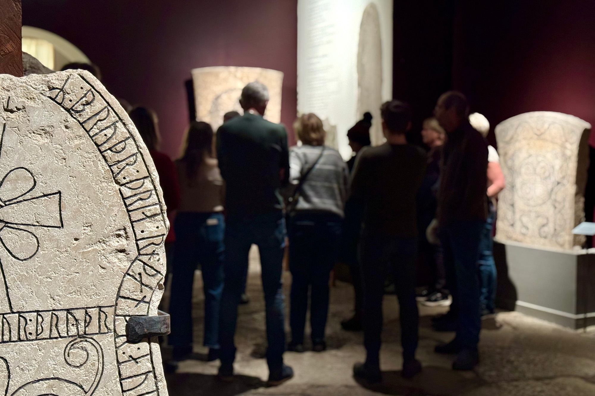 En bildsten i förgrunden. Ett museum. Bakom: siluetter av en grupp människor.
