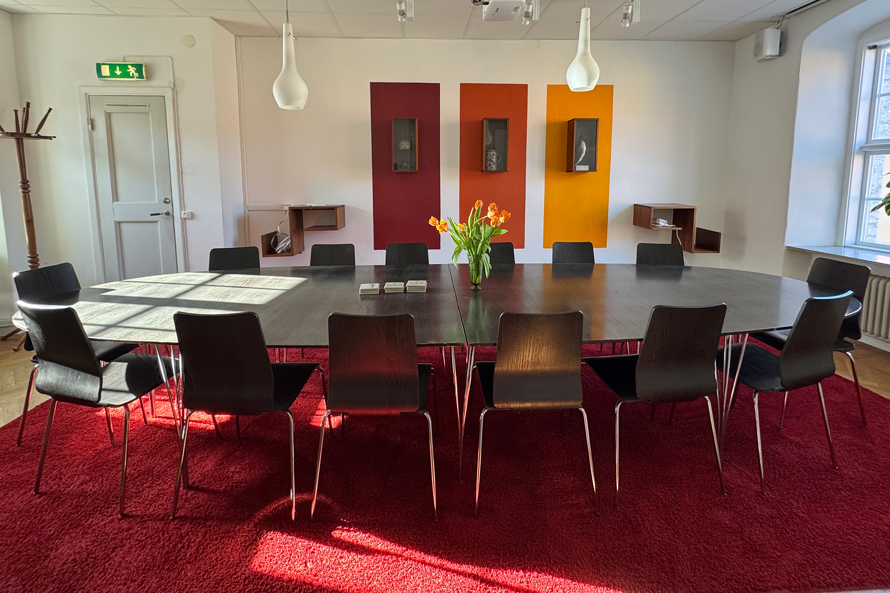 Ett konferensrum. Avlångt svart bord. Stolar runt. Tulpaner på bordet.