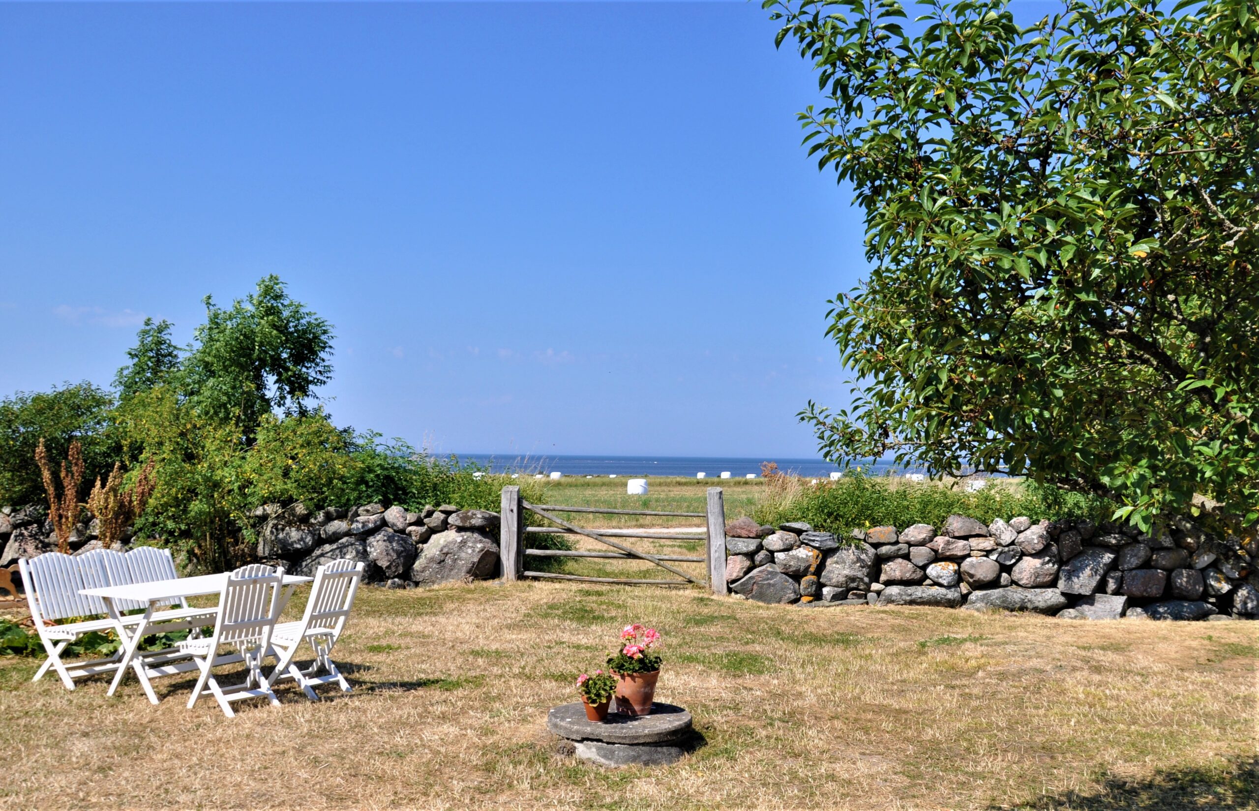 Trädgårdsmöbler, stenmur, havet bakom.