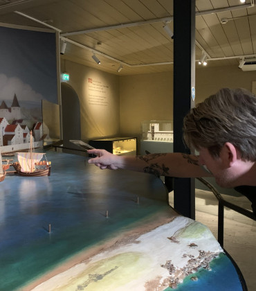 En guide som pekar på en modell med hus, i ett museum.